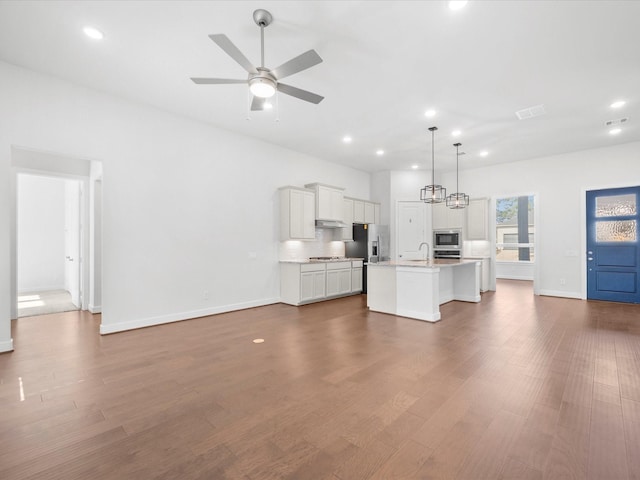 kitchen with pendant lighting, appliances with stainless steel finishes, dark wood-type flooring, and an island with sink