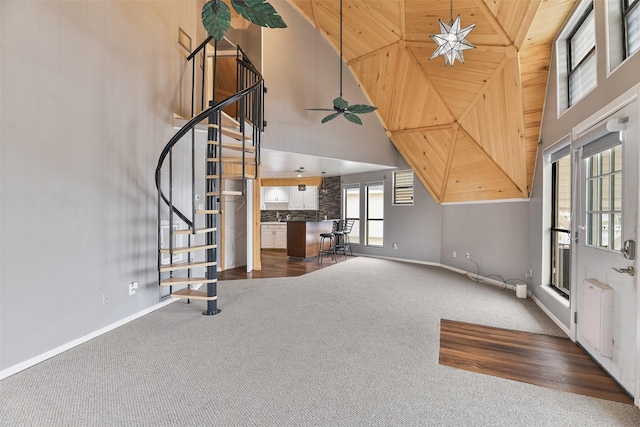 unfurnished living room with ceiling fan, high vaulted ceiling, wood ceiling, and dark colored carpet