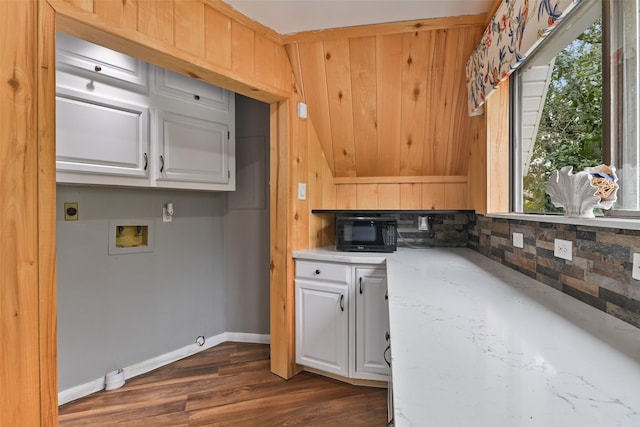 kitchen featuring white cabinets, light stone counters, dark wood-type flooring, and wooden walls