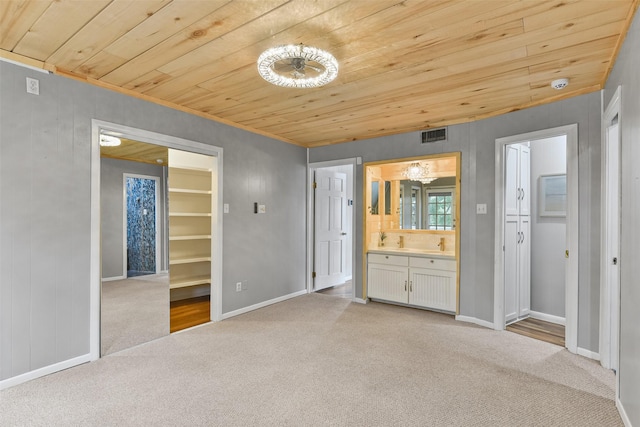 unfurnished bedroom with ensuite bathroom, wooden ceiling, a spacious closet, and light carpet