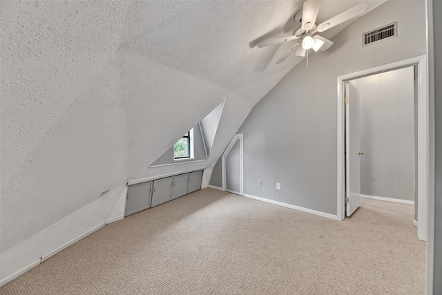 additional living space with vaulted ceiling, light carpet, ceiling fan, and a textured ceiling