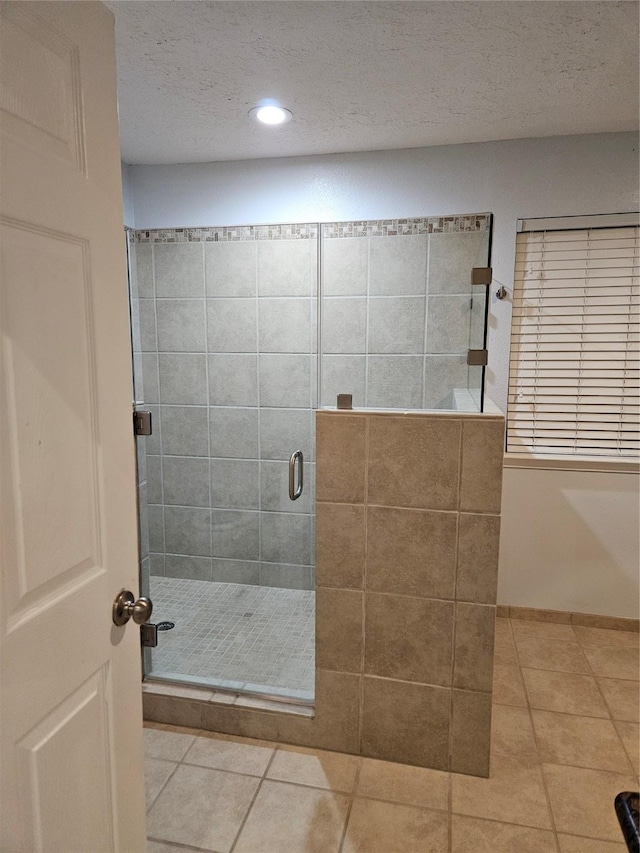 bathroom with tile patterned floors, a shower with shower door, and a textured ceiling