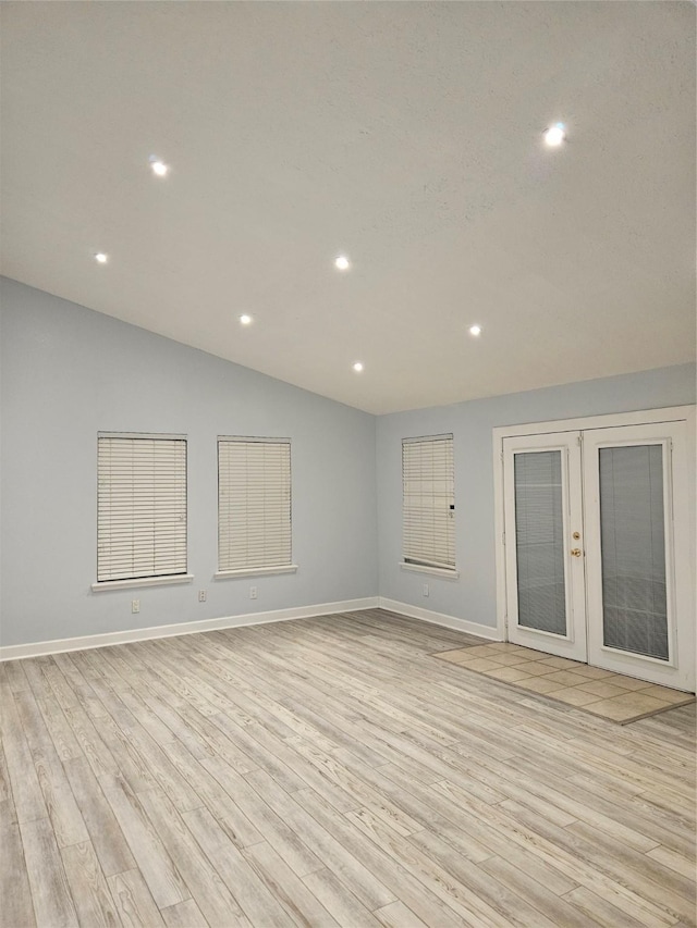 empty room featuring lofted ceiling, light wood-type flooring, and french doors