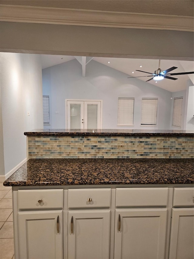 interior space featuring backsplash, dark stone countertops, crown molding, lofted ceiling, and white cabinets