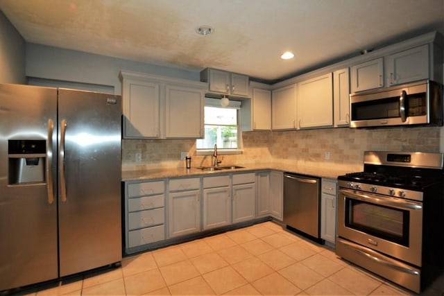 kitchen featuring sink, tasteful backsplash, gray cabinets, light tile patterned floors, and appliances with stainless steel finishes