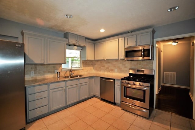 kitchen with gray cabinetry, sink, decorative backsplash, light tile patterned floors, and stainless steel appliances