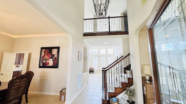 tiled entryway featuring crown molding, plenty of natural light, and a high ceiling