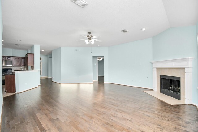 unfurnished living room with a tile fireplace, ceiling fan, sink, light hardwood / wood-style flooring, and lofted ceiling