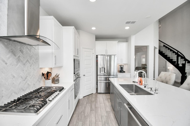 kitchen with sink, wall chimney exhaust hood, stainless steel appliances, decorative backsplash, and white cabinets