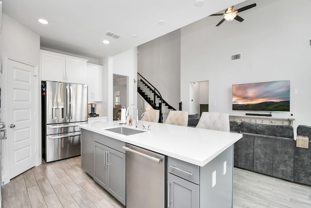 kitchen featuring gray cabinetry, a center island with sink, sink, ceiling fan, and stainless steel appliances