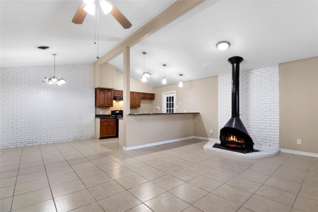 unfurnished living room with brick wall, ceiling fan with notable chandelier, light tile patterned floors, vaulted ceiling with beams, and a wood stove