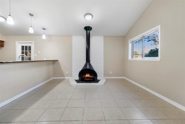 unfurnished living room featuring sink, a wood stove, lofted ceiling, and light tile patterned flooring