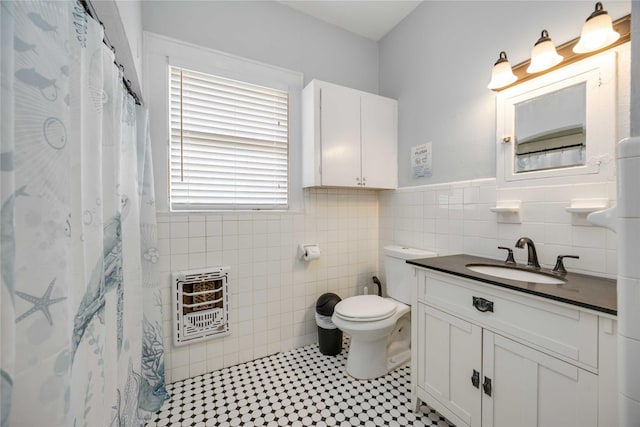 bathroom featuring heating unit, vanity, tile walls, and toilet