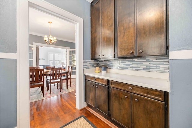 kitchen featuring hanging light fixtures, ornamental molding, a notable chandelier, dark hardwood / wood-style flooring, and dark brown cabinetry