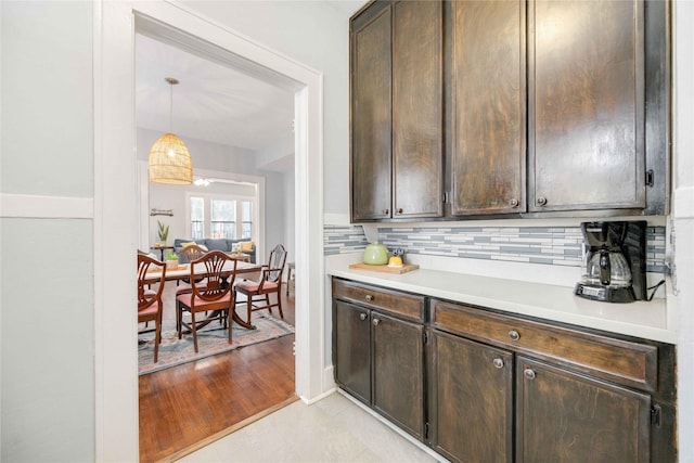 kitchen with decorative backsplash, pendant lighting, light hardwood / wood-style floors, and dark brown cabinets