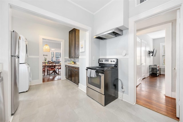 kitchen featuring light wood-type flooring, stainless steel electric stove, stacked washer and clothes dryer, and wall chimney exhaust hood