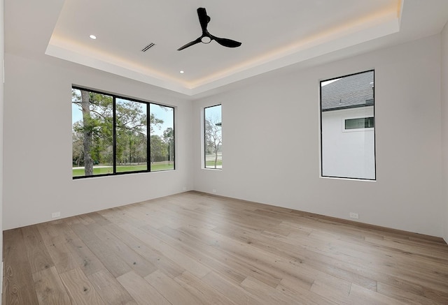 unfurnished room featuring ceiling fan, light hardwood / wood-style flooring, and a tray ceiling