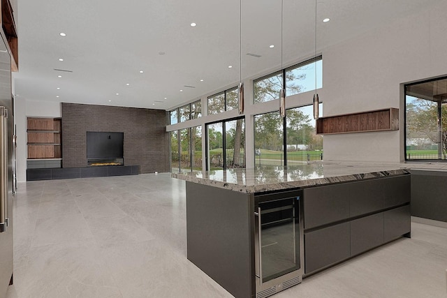 kitchen featuring light stone countertops, a towering ceiling, beverage cooler, a kitchen island, and a tiled fireplace