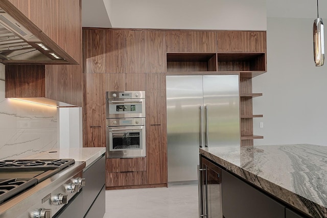 kitchen with pendant lighting, exhaust hood, appliances with stainless steel finishes, stone countertops, and beverage cooler