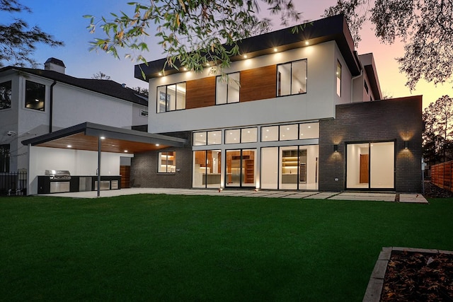 back house at dusk featuring a yard, a patio area, and exterior kitchen