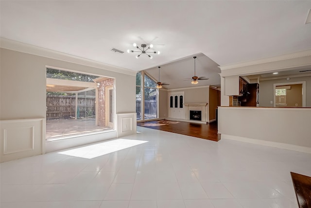 unfurnished living room featuring ceiling fan with notable chandelier, light tile patterned floors, vaulted ceiling, and ornamental molding