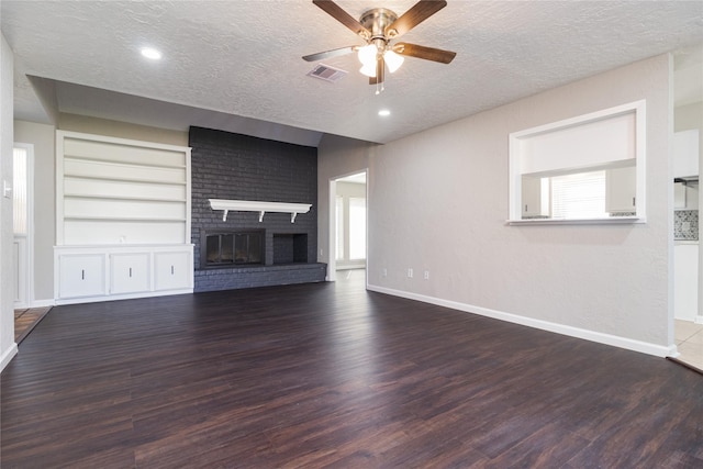 unfurnished living room with built in features, dark wood-type flooring, a textured ceiling, and a brick fireplace