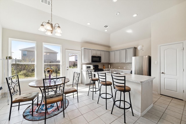 kitchen featuring gray cabinets, stainless steel refrigerator, a kitchen island with sink, and a healthy amount of sunlight