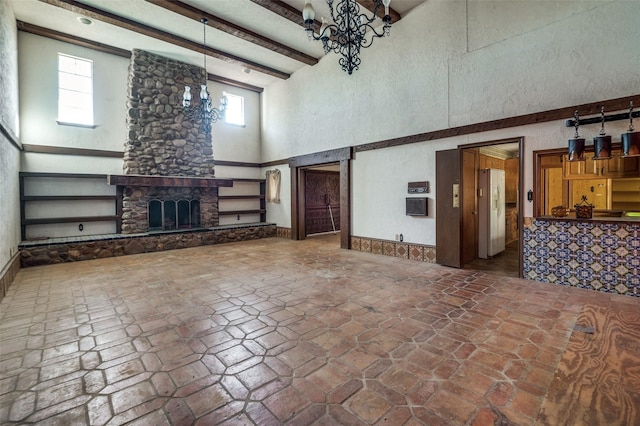 unfurnished living room featuring beamed ceiling, a notable chandelier, a stone fireplace, and a towering ceiling