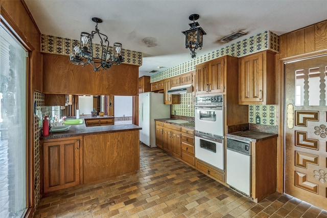 kitchen featuring a healthy amount of sunlight, white appliances, kitchen peninsula, and a chandelier