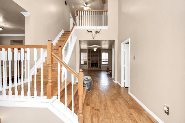 foyer with ceiling fan, a brick fireplace, a towering ceiling, wood-type flooring, and ornamental molding