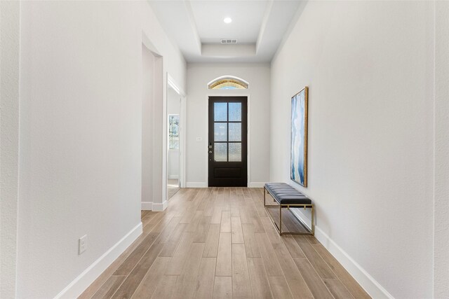 entryway with a tray ceiling and light wood-type flooring