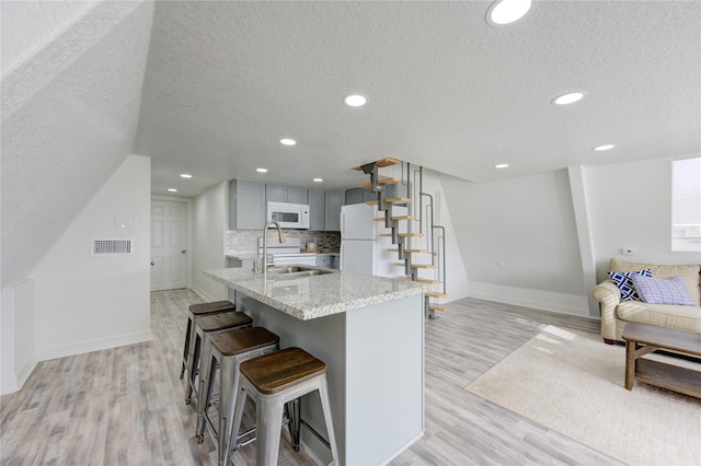 kitchen with a textured ceiling, sink, white appliances, and light wood-type flooring