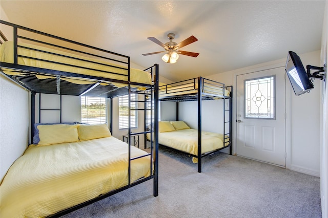 carpeted bedroom featuring ceiling fan, a textured ceiling, and multiple windows