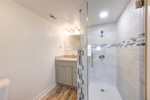 bathroom featuring vanity, toilet, a textured ceiling, walk in shower, and wood-type flooring