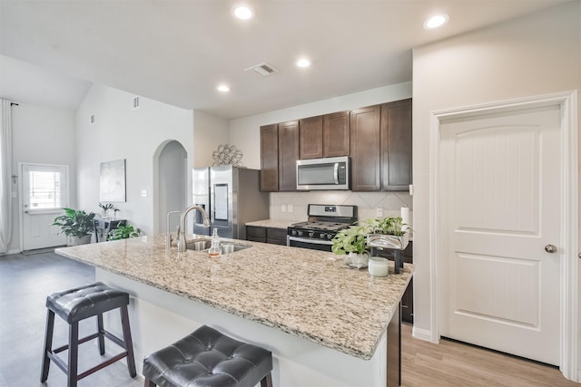 kitchen featuring a kitchen bar, appliances with stainless steel finishes, dark brown cabinetry, a kitchen island with sink, and sink