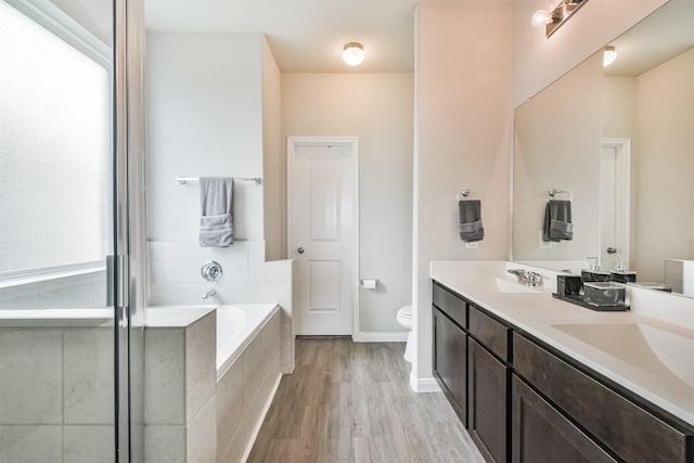 bathroom with tiled tub, hardwood / wood-style floors, vanity, and toilet