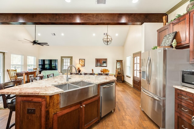 kitchen featuring light wood-type flooring, ceiling fan with notable chandelier, stainless steel appliances, a kitchen island with sink, and sink