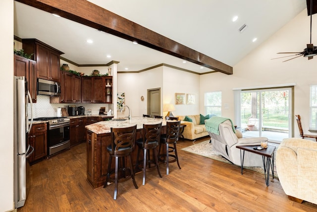 kitchen with backsplash, dark wood-type flooring, an island with sink, light stone counters, and stainless steel appliances