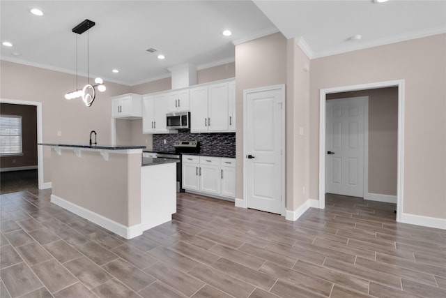 kitchen featuring white cabinets, appliances with stainless steel finishes, decorative light fixtures, and a kitchen island with sink