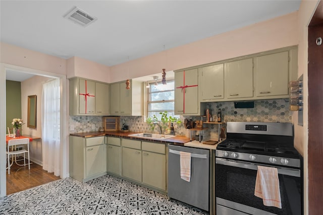 kitchen with sink, green cabinetry, decorative backsplash, light wood-type flooring, and appliances with stainless steel finishes