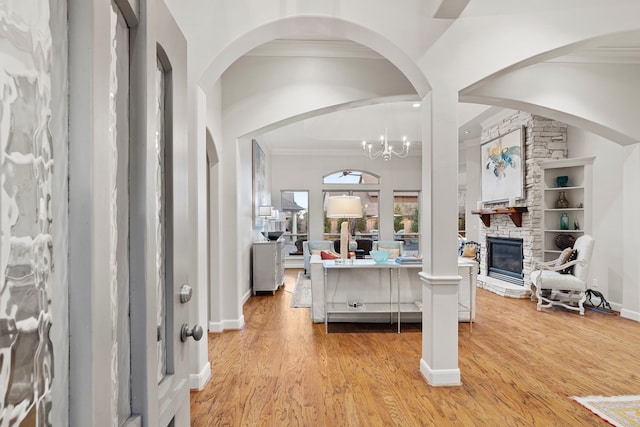 entrance foyer featuring ornamental molding, a stone fireplace, a notable chandelier, and light hardwood / wood-style flooring