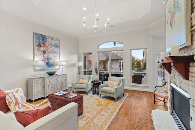 living room with crown molding, a stone fireplace, a notable chandelier, and light wood-type flooring