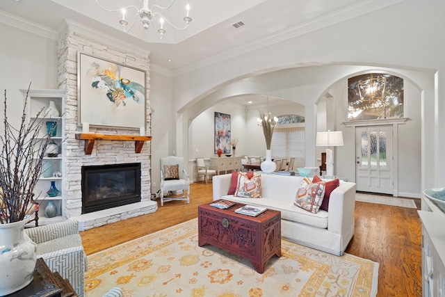 living room with crown molding, a stone fireplace, light hardwood / wood-style floors, and a notable chandelier