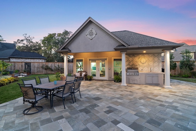 patio terrace at dusk with area for grilling, sink, french doors, and exterior kitchen