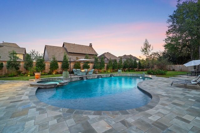 pool at dusk featuring a patio area, pool water feature, and an in ground hot tub