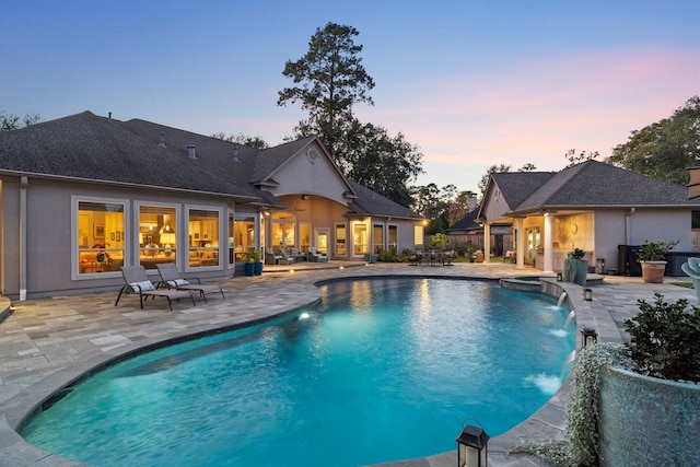 pool at dusk featuring pool water feature and a patio area