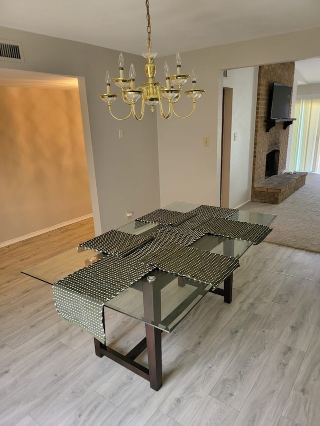 unfurnished dining area with a chandelier, light wood-type flooring, and a brick fireplace