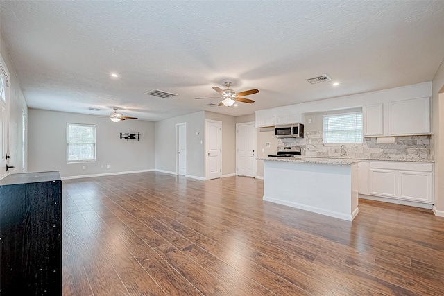 kitchen featuring appliances with stainless steel finishes, a textured ceiling, decorative backsplash, white cabinets, and hardwood / wood-style flooring