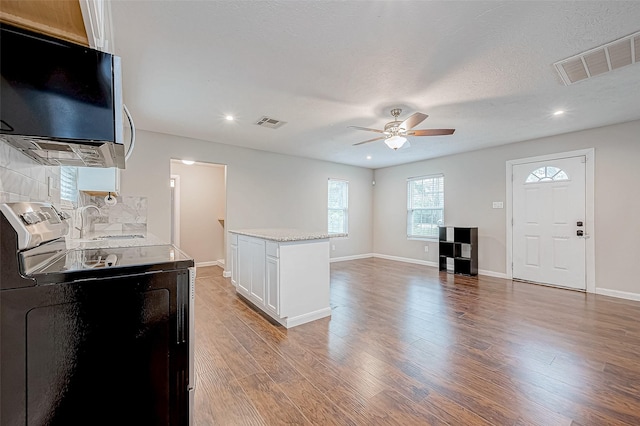 kitchen featuring light wood-type flooring, stainless steel electric stove, sink, white cabinets, and a kitchen island