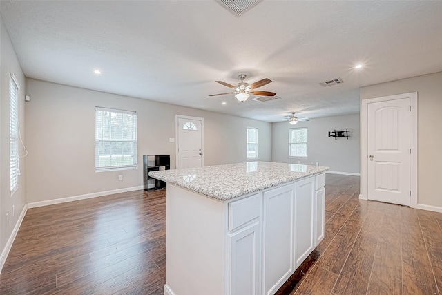 kitchen featuring ceiling fan, a center island, light stone counters, dark hardwood / wood-style floors, and white cabinets